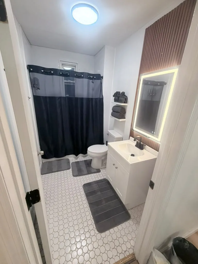 Small bathroom with hex tile floor, LED mirror and fresh bath mats after cleaning
